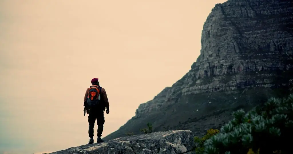 A hiker standing on a rocky ledge, looking up at a mountain