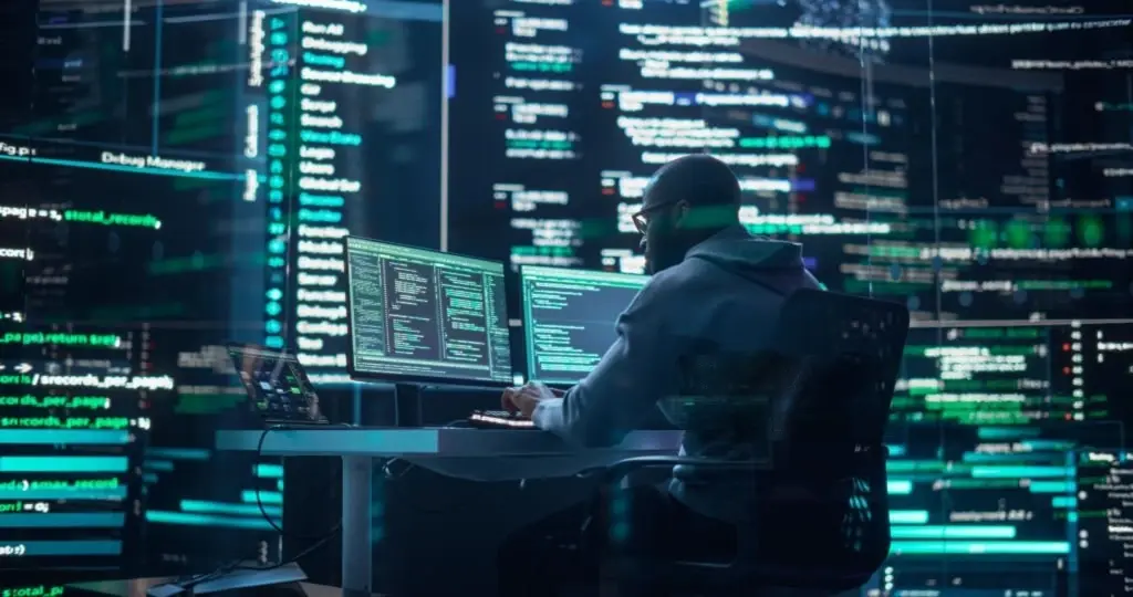 An engineer at a workstation surrounded by screens of code