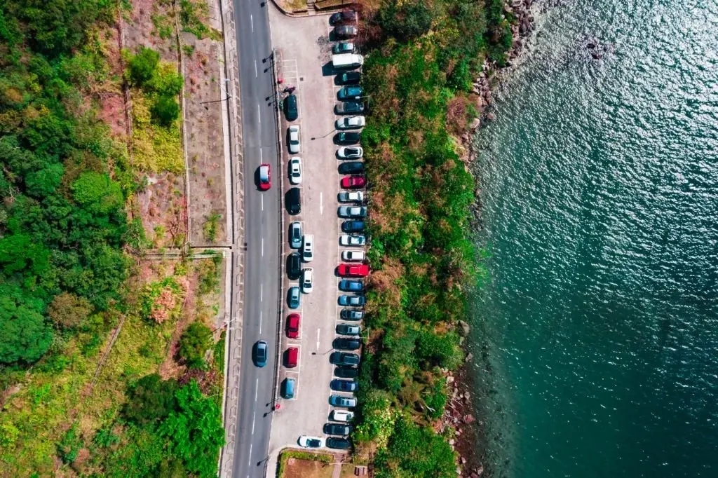 Aerial view of cars parked along a coastal road beside the sea